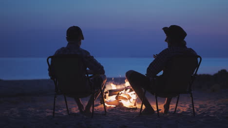 Dos-Amigos-De-Un-Adolescente-Están-Sentados-Junto-Al-Fuego-Relajándose-Y-Hablando-En-Vivo-Chat-Adolescente