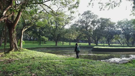 young woman with backpack walking alone on a peaceful park with pond