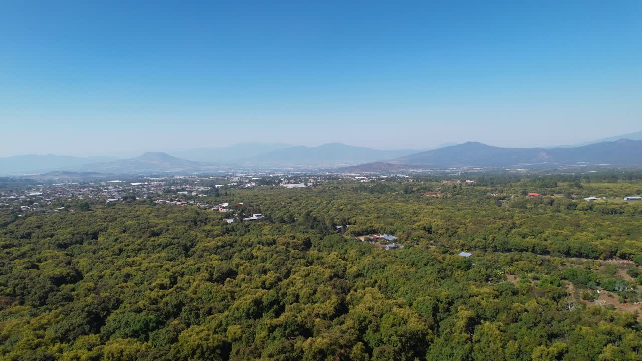 멕시코 미초아칸의 산과 작은 마을이 내려다보이는 경치 좋은 녹색 아보카도 나무 위로 느린 공중 오른쪽 팬
