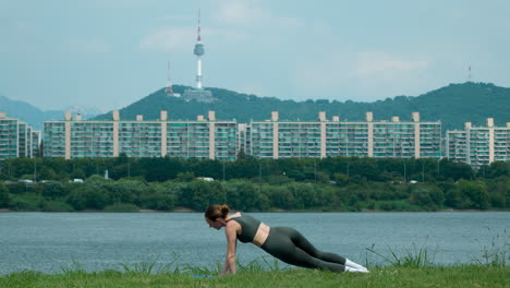 young female trainer practice hatha yoga instructor training outside, vasishthasana side plank, arm and leg support balancing pose, healthy lifestyle at han river park in seoul city, view of namsan