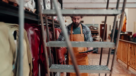 Tablet,-leather-workshop-and-man-on-steps-at-shelf