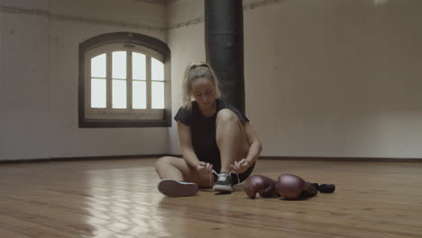 long shot of young woman lacing up sneakers in kickboxing gym