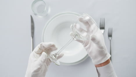 professional table setting with white gloves. plates, fork, knife, and glass arranged on a white table.