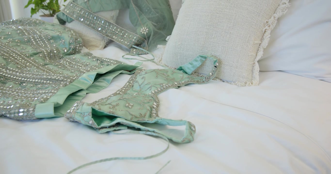 Camera is panning right toward bed, revealing embellished mint dress and dupatta to showcase bodice