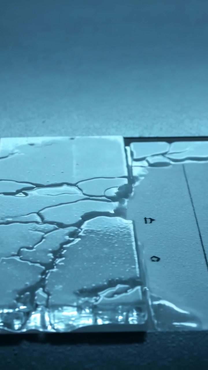 Vertical video: Spreading clear liquid from pools across cracked panel seam on mat, wetting cracks