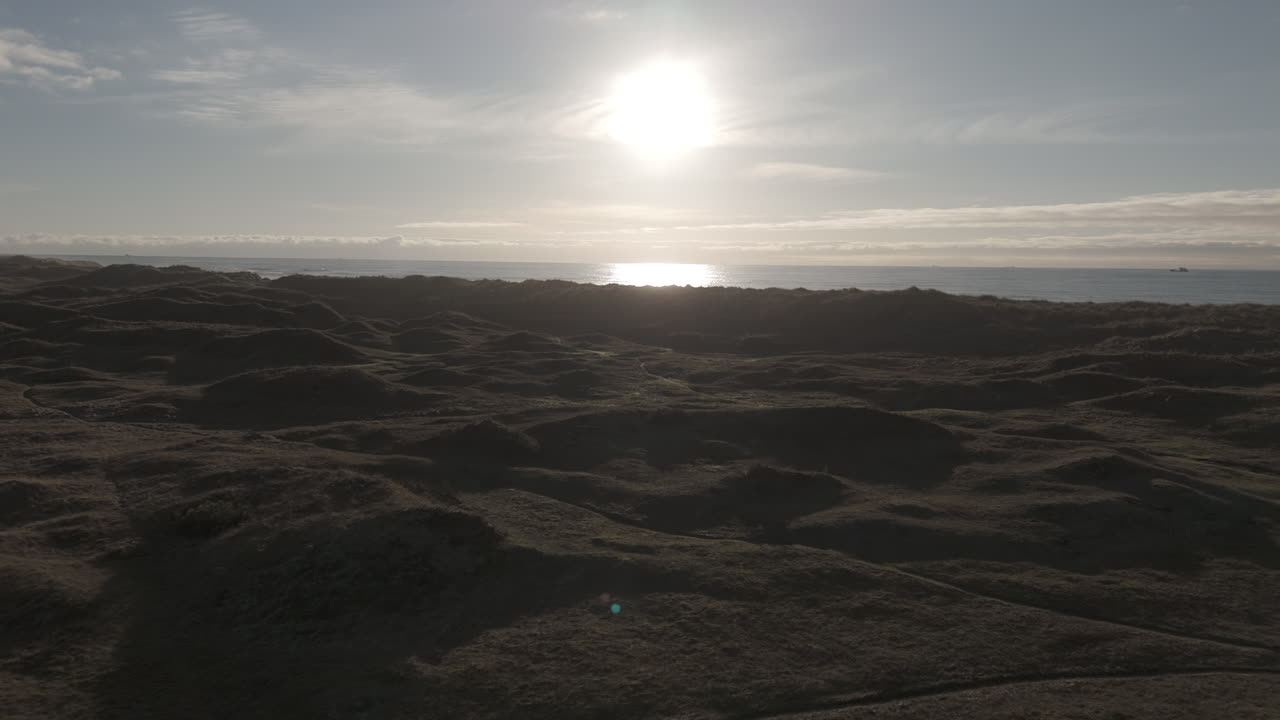 Forward flying drone shot over the dunes near Borestranda Norway during sunset going towards the beach and sea and ending tilted downwards over the waves LOG