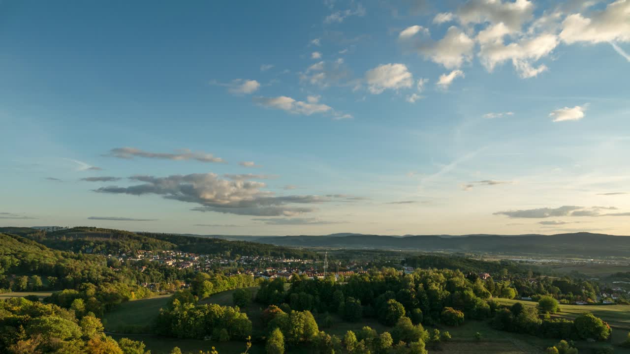 Bewegte Zeitrafferaufnahme eines Sonnenuntergangs über bewaldeten Hügeln und Dörfern.