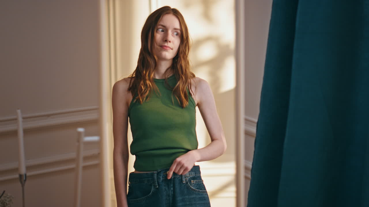 클로즈업 은 소녀는 반사 된 오래된 청바지를 시도합니다. 불행한 슬픈 여성은 체중을 잃습니다.