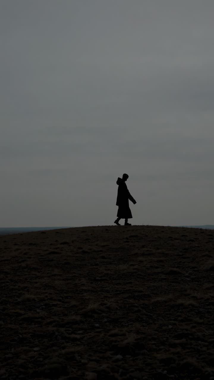 Silhouette of a person walking on a hilltop, captured from a low angle