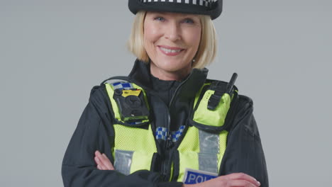 full length studio portrait of smiling mature female police officer against plain background