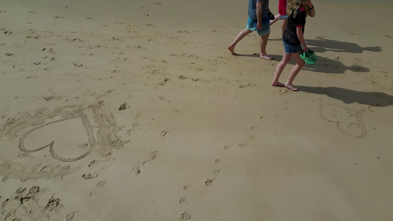 Family walking down sandy beach, heart shape sand drawing Algarve Portugal