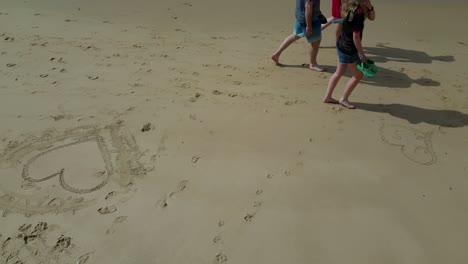 family walking down sandy beach, heart shape sand drawing algarve portugal