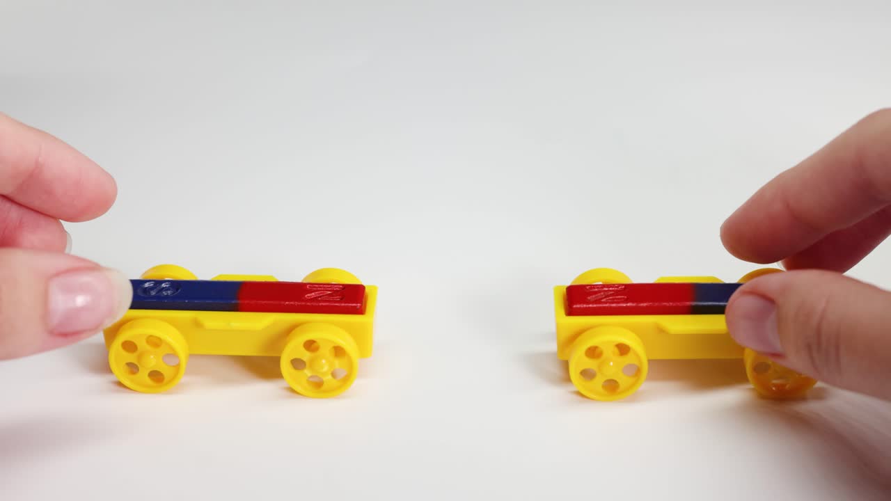Hands manipulate magnetic toy cars on a white surface, illustrating magnetic attraction and repulsion with colorful components