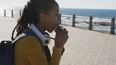 African-american-woman-sitting-eating-sandwich-promenade-by-the-sea