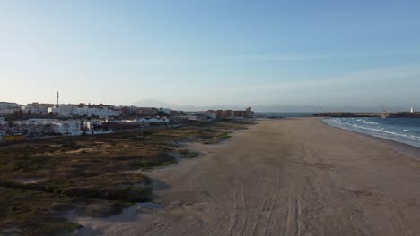 Las-Arenas-Azotadas-Por-El-Viento-De-Tarifa-Se-Extienden-Interminablemente-Bajo-Un-Vasto-Cielo-Azul,-Encontrándose-Con-Las-Olas-Del-Atlántico-Y-La-Silueta-Distante-De-África.