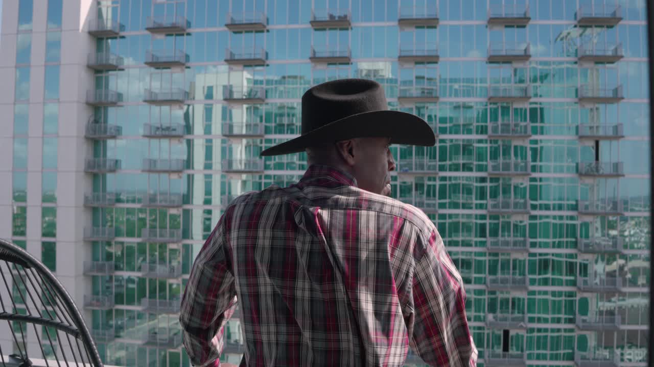 Uomo di colore con cappello da cowboy nero che guarda da un balcone.