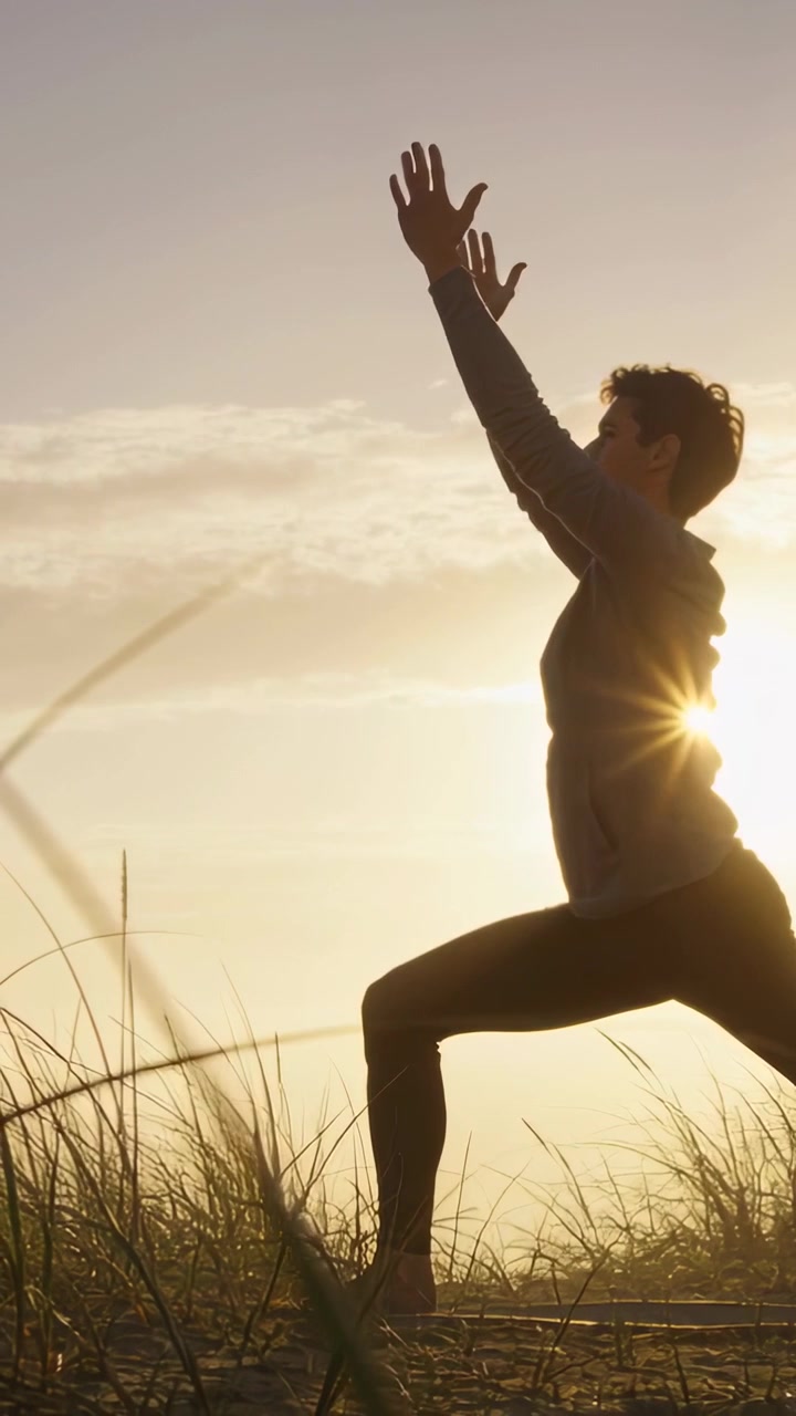 Video verticale: Donna in abbigliamento da yoga che mantiene un affondo e allunga le braccia sulle dune mentre il sole scivola oltre il busto