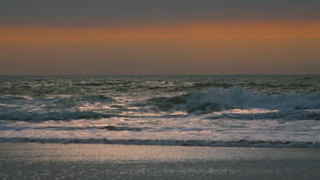hypnotic contrast waves crashing on beach in slow motion with orange sunlight background and reflections on shoreline. prores 4k.