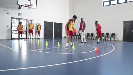 basketball players practicing dribbling skills in gym with coach observing