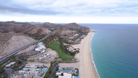 Aerial-view-over-the-beautiful-coastal-landscape-of-Marquis-los-cabos-overlooking-the-luxurious-hotel-los-cabos-and-private-villas-right-on-the-beach-with-blue-sea-and-mountains-in-the-background