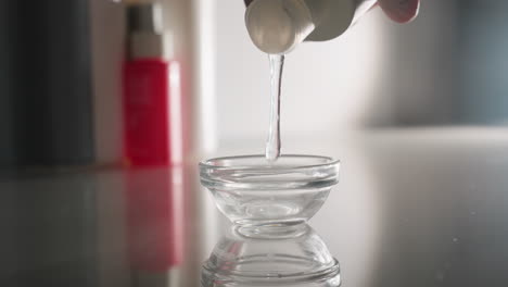 massage therapist wearing gloves pours golden oil into small white bowl on trolley against blurred spa background conveying preparation ritual for soothing facial and full body treatment session