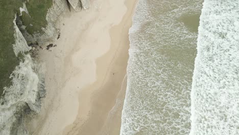 sea waves crashing on sandy shore of white rocks beach with limestone cliffs and cave near portrush in northern ireland