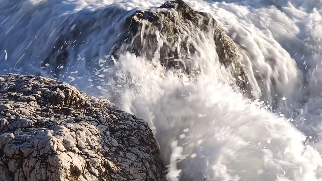 piedra salpicada por las olas del mar, espumando en la orilla de la playa salvaje en la costa mediterránea en la hora dorada