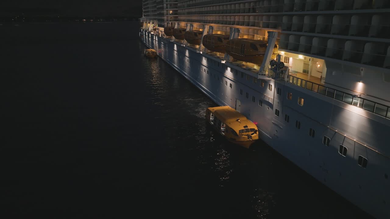 Aerial drone rotating shot over tender boats unloading and loading passengers on a cruise ship at night time