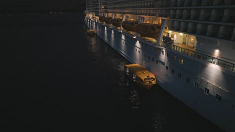 aerial drone rotating shot over tender boats unloading and loading passengers on a cruise ship at night time