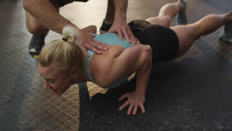 entrenador masculino corrigiendo la forma de la mujer caucásica en forma mientras hace ejercicios de empuje en el gimnasio