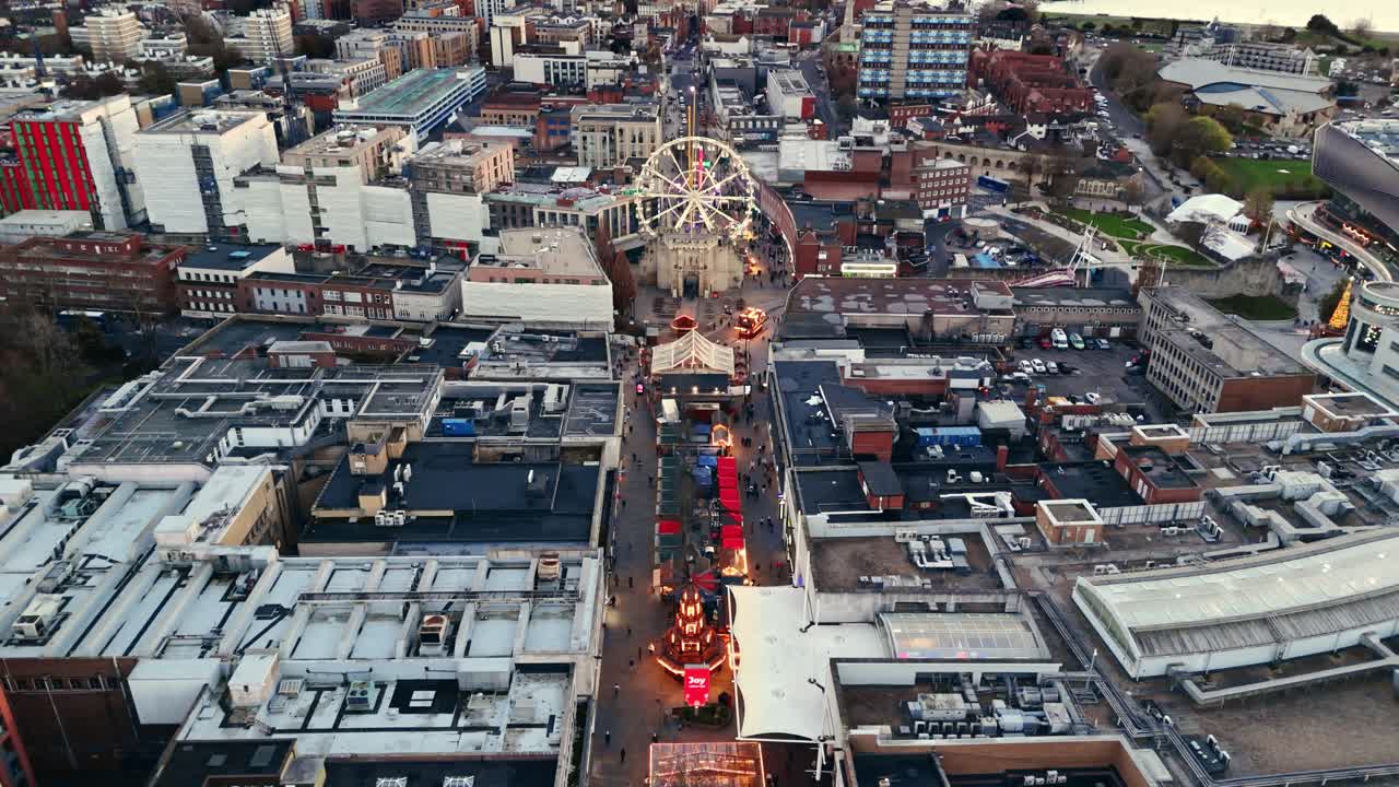 Drone shot descending over Southampton Christmas Market at sunset, revealing glowing festive stalls, a bright ferris wheel, and crowds exploring as warm evening light spreads across the lively city