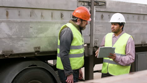 boss and worker wearing vests and safety helmets organizing a truck fleet in a logistics park while they consulting a document 8