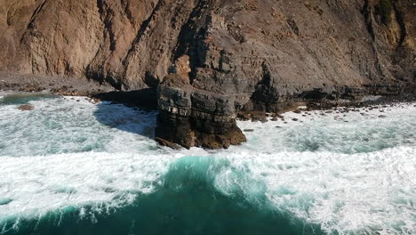 Aerial-done-shot-of-whitewater-waves-hitting-a-cliff-on-the-shore-of-a-beach-in-Algarve,-Portugal