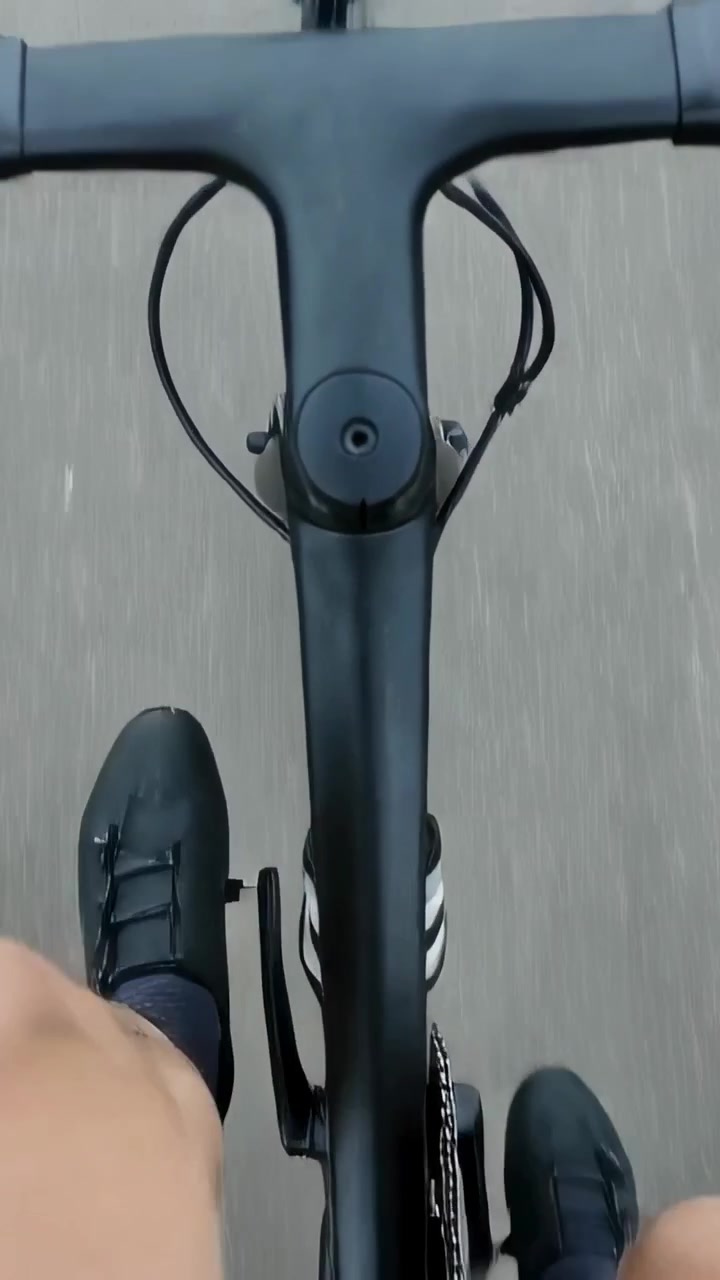 Video verticale: Ciclista che aggancia le tacchette, con scarpe da ciclismo e manubrio, mentre percorre una strada nebbiosa.