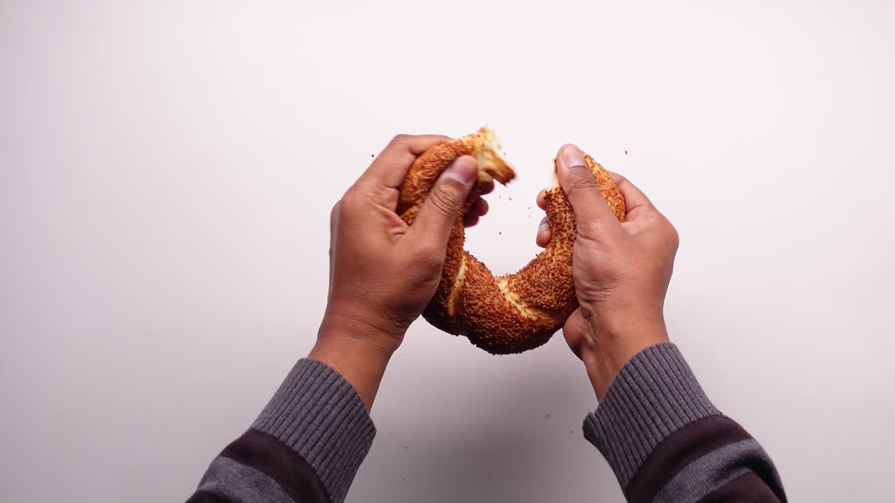 Hænder deler en frisk simit på en hvid baggrund