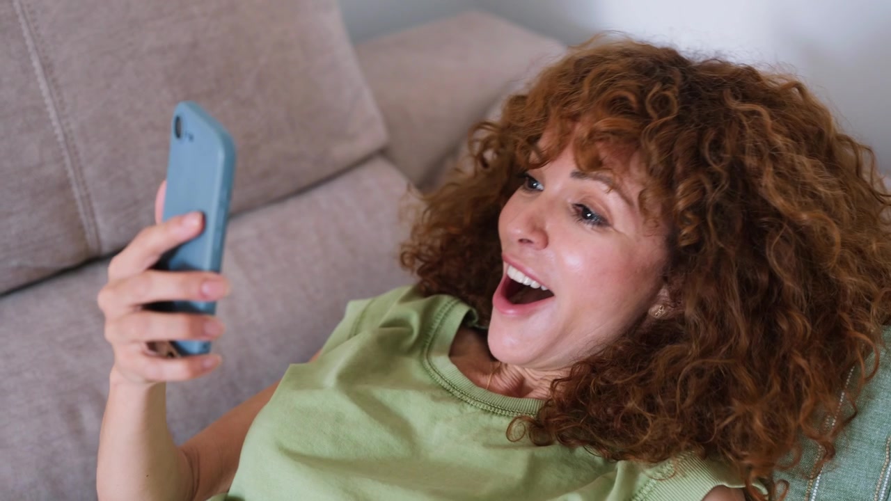 Happy Woman Using Smartphone While Relaxing on Sofa