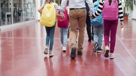 Vertical motion of a group of multiethnic pupils with teachers walking in school hallway and talking together