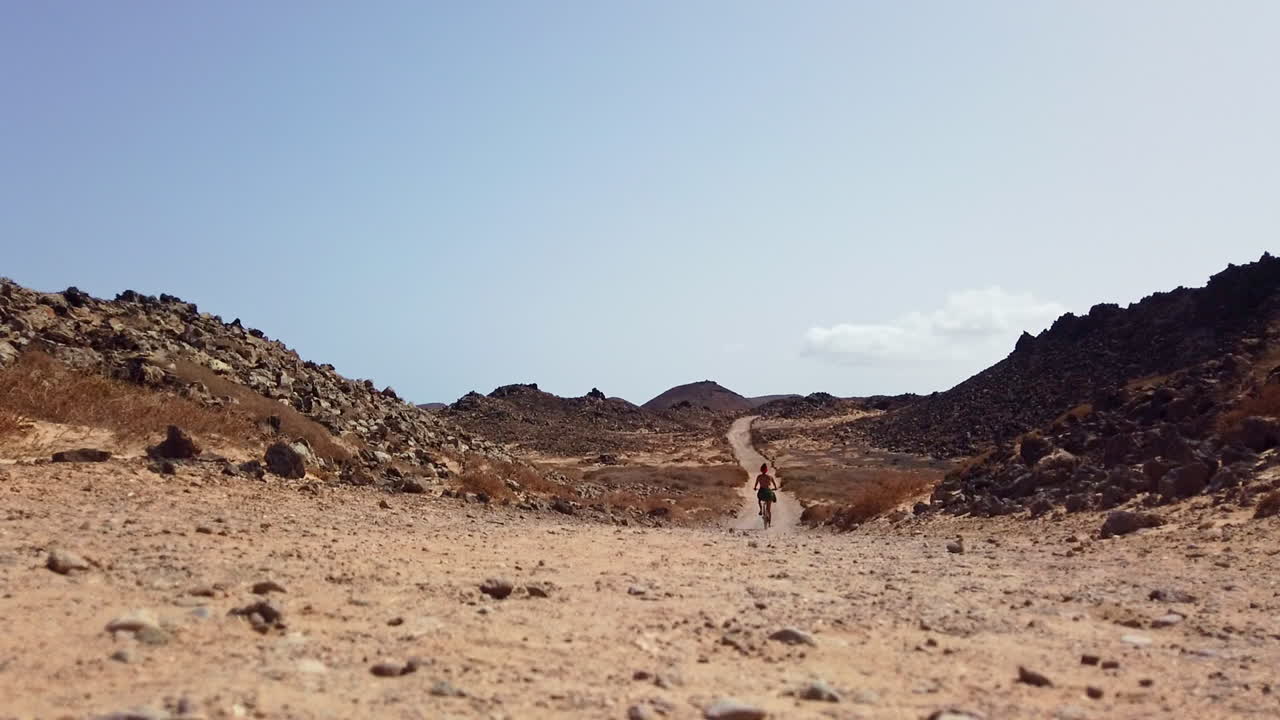 한 여자가 로보스 섬의 따뜻한 날씨에 돌로 된 길을 자전거로 달리고 있습니다.