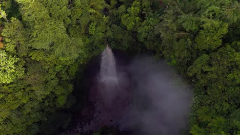 drone view captures nungnung waterfall nestled in a dense jungle landscape where steam rises and the sound of rushing water echoes through vibrant green surroundings in remote bali nature