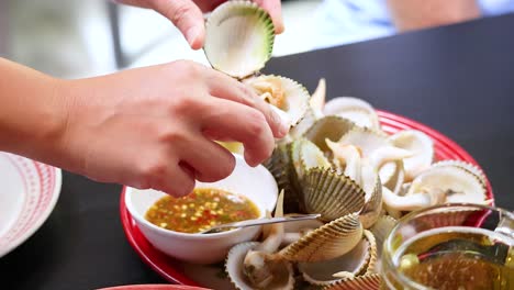 person enjoying boiled clams with dipping sauce and beer in phuket