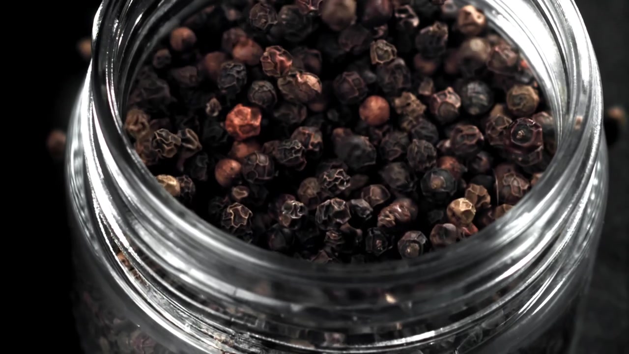 Hele svarte pepperkorn som faller og fyller et glass