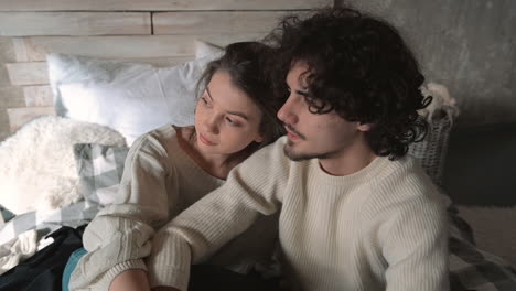 young romantic couple sitting in bed wearing winter clothes and talking hugging