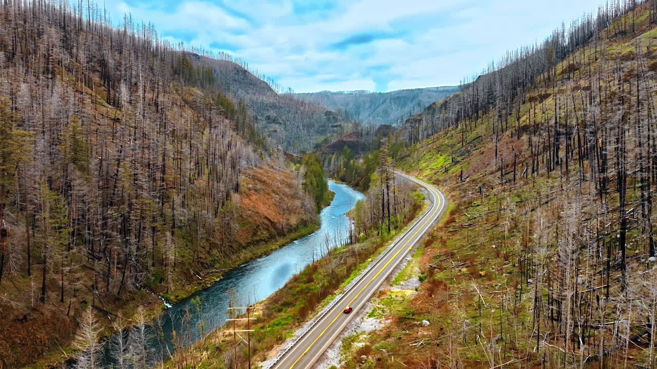 Car rides by the highway in the mountains above the river. Rocky landscape covered by dry forest. Top view.