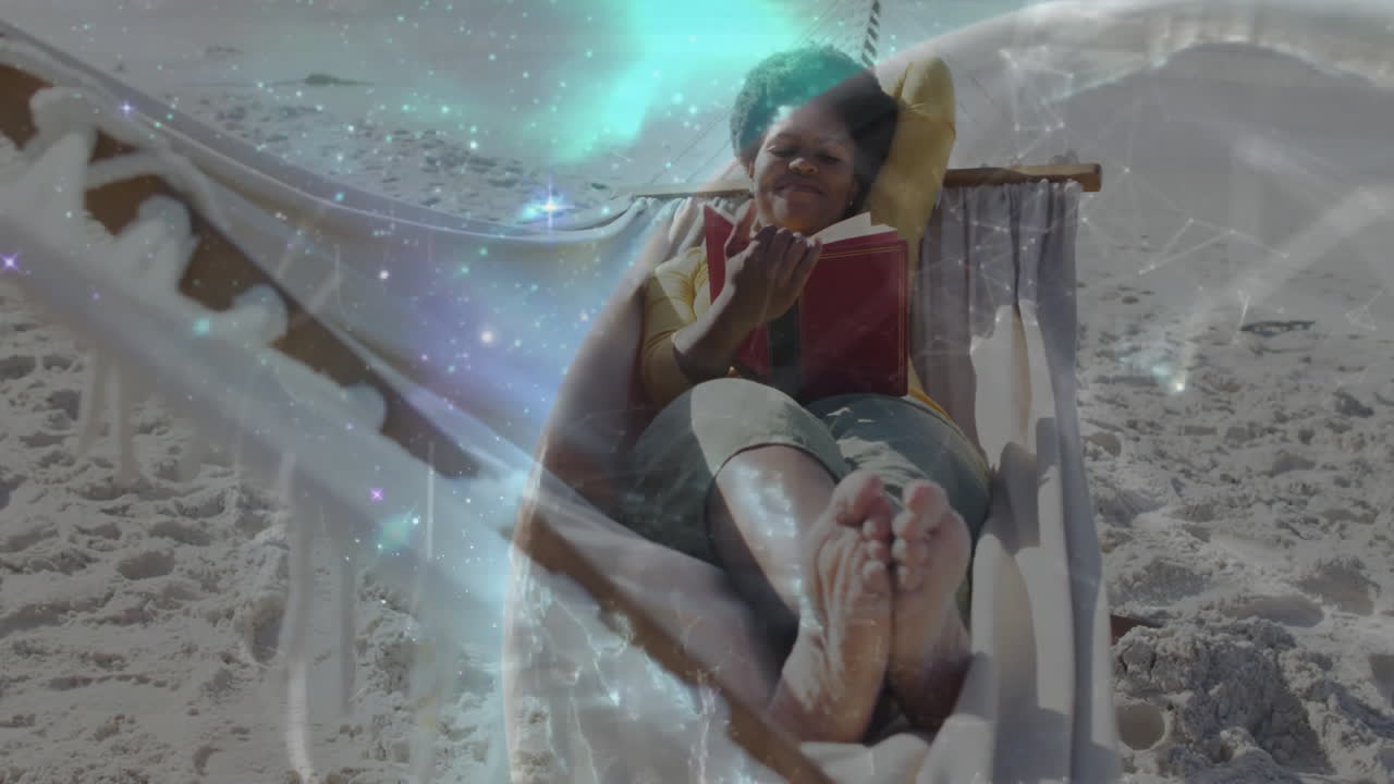 Woman reclining in beach hammock, reading red book with stars and aurora for education