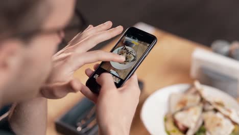 close-up de mãos masculinas segurando smartphone e tirando fotos de comida na mesa no restaurante