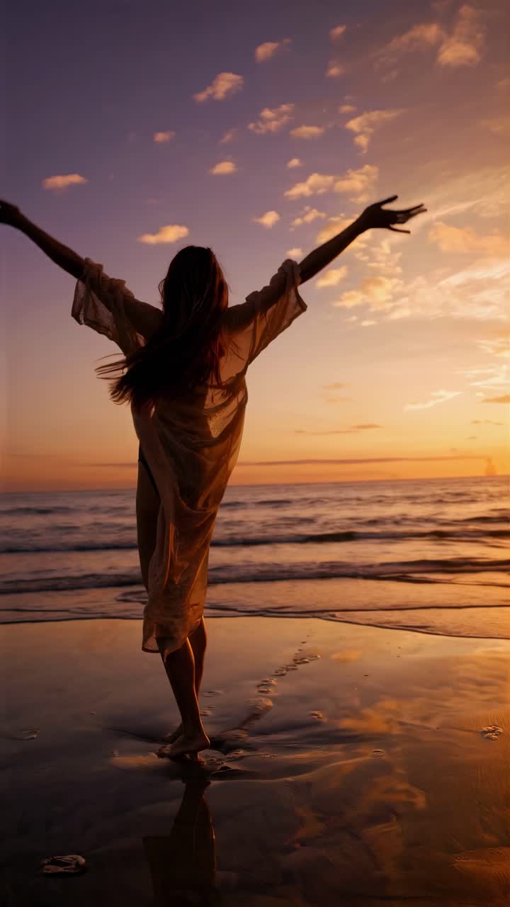 Silhouette of a woman with arms outstretched on a beach at sunset, captured from a low angle