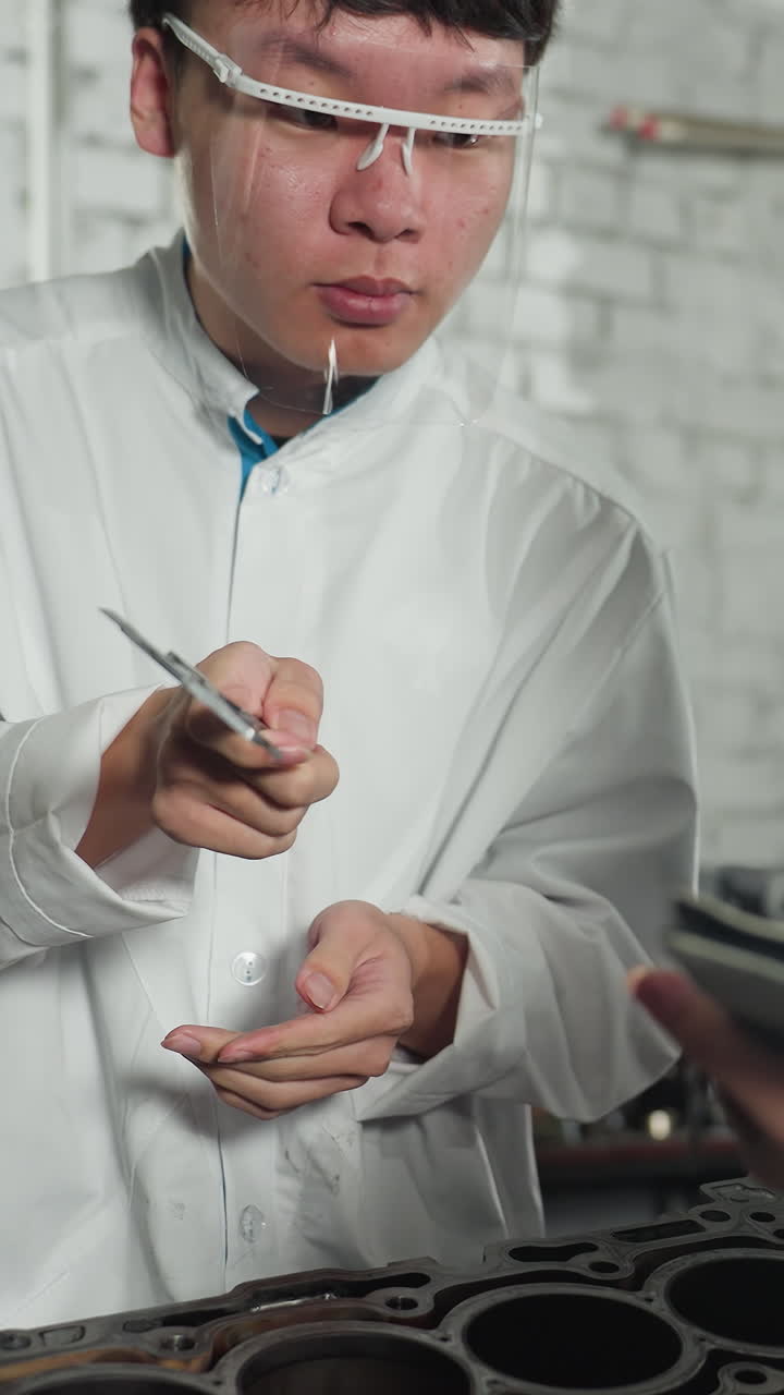 산업 작업실에서 기계 공학자가 동료에게 읽기를 보여주는 동안 베르니에 칼리퍼를 사용하여 엔진 두께를 신중하게 측정합니다.