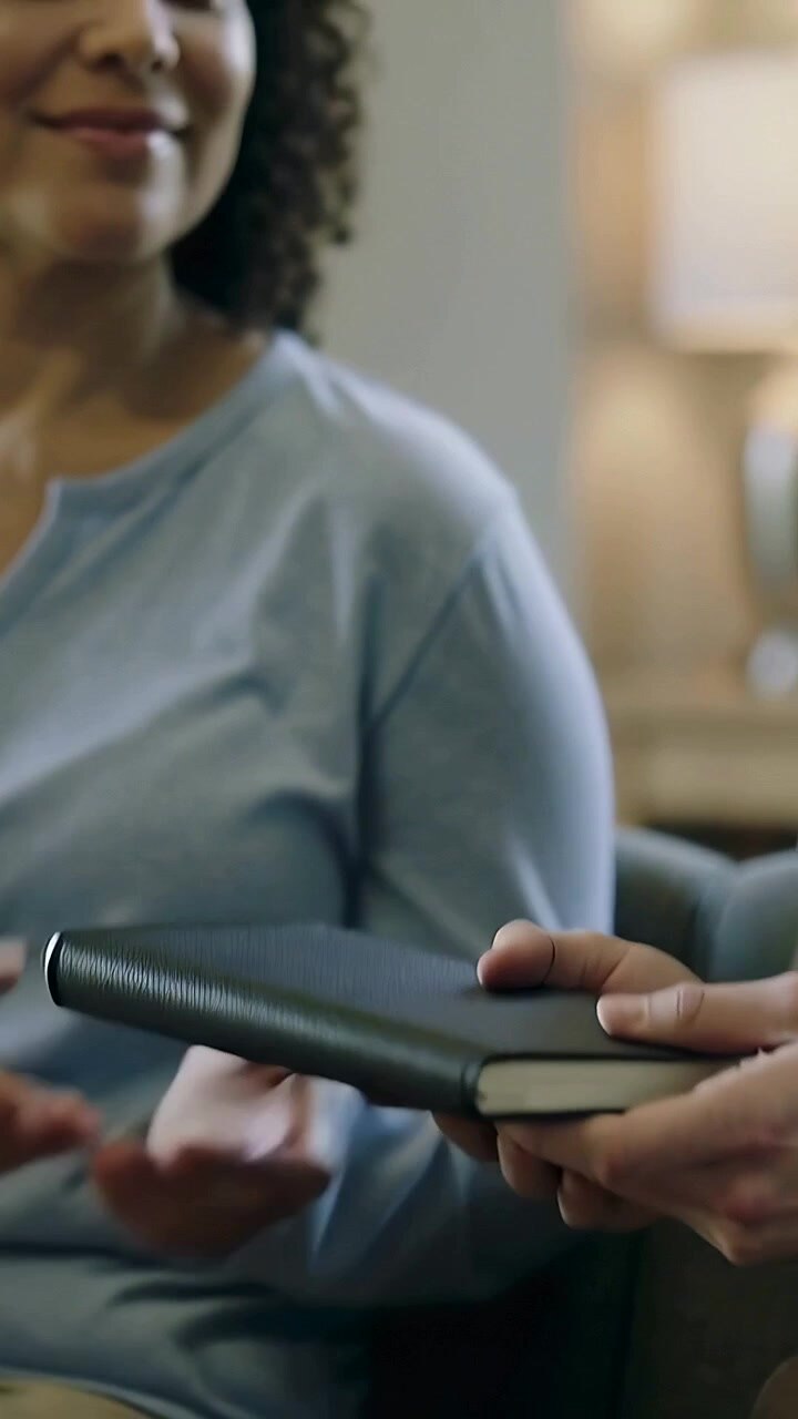 Vertical video: Lifting notebook woman in blue top passing it to partner on sofa, sharing