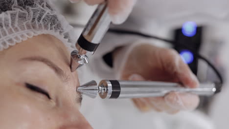 la doctora esteticista hace a la mujer micro corrientes terapia facial usando impulsos eléctricos en el salón de spa