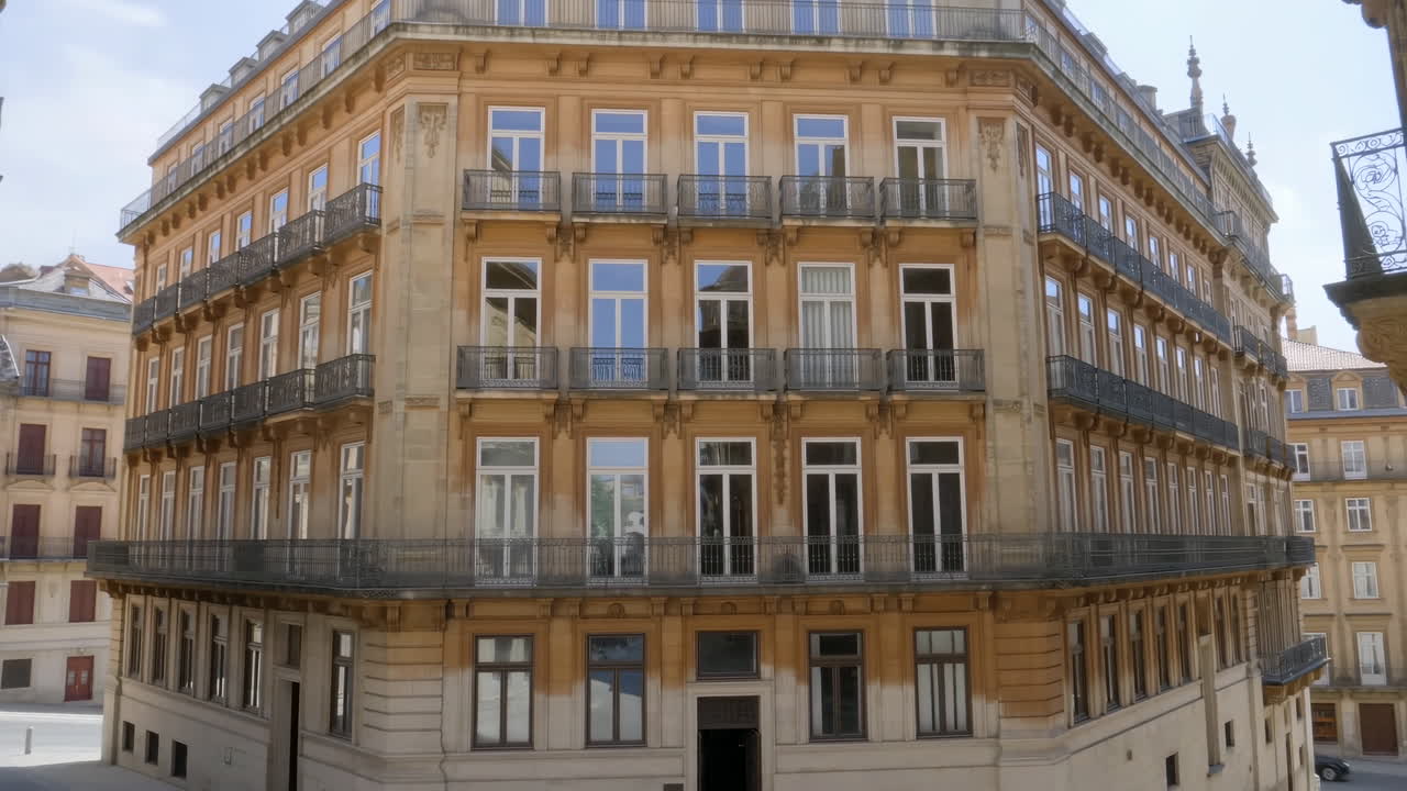 Edificio angolare europeo illuminato dal sole con balconi, facciata neoclassica in arenaria che si affaccia su una piazza vuota, finestre a ghigliottina alte